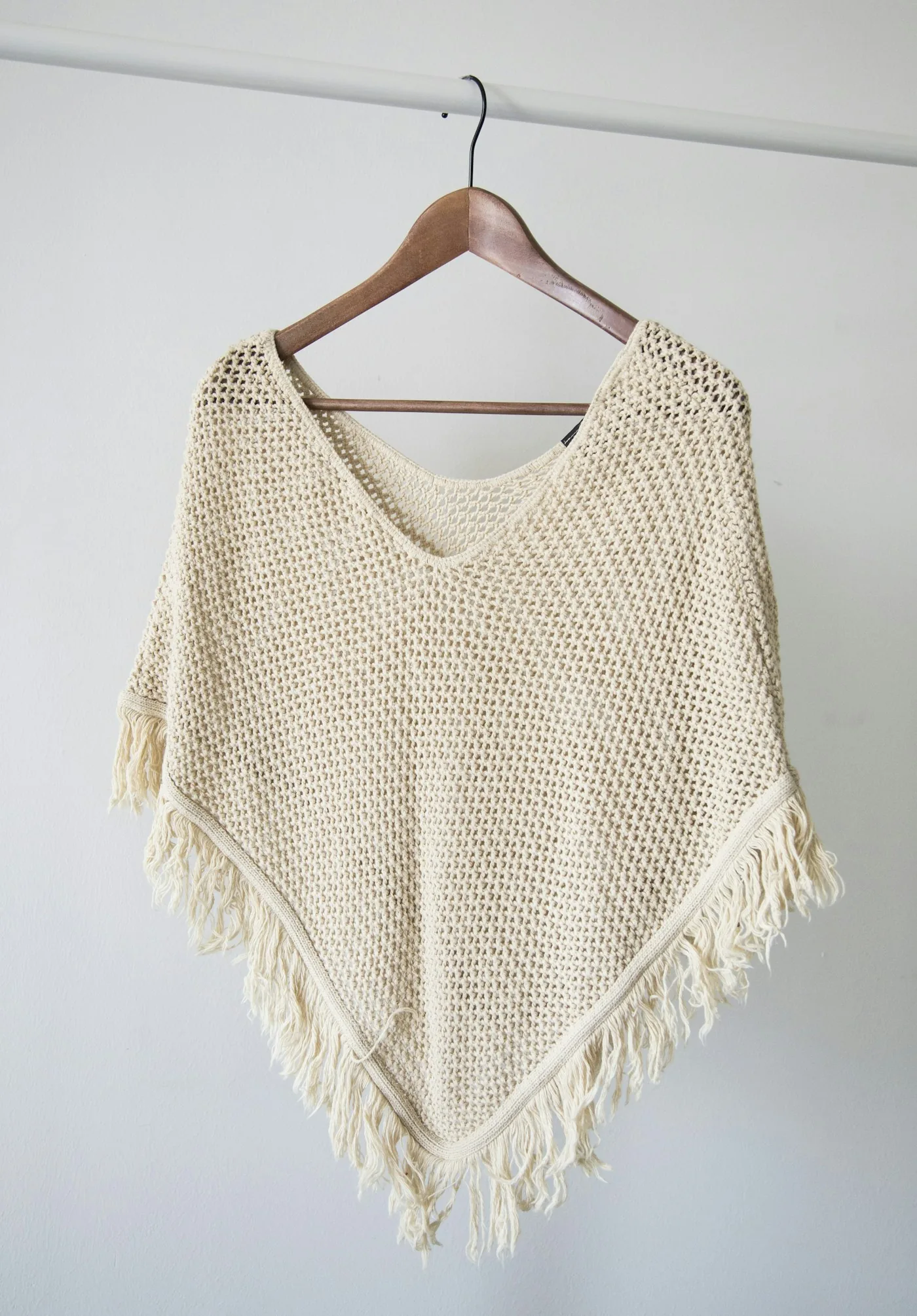 Cream knitted garment with fringe hanging on a rail