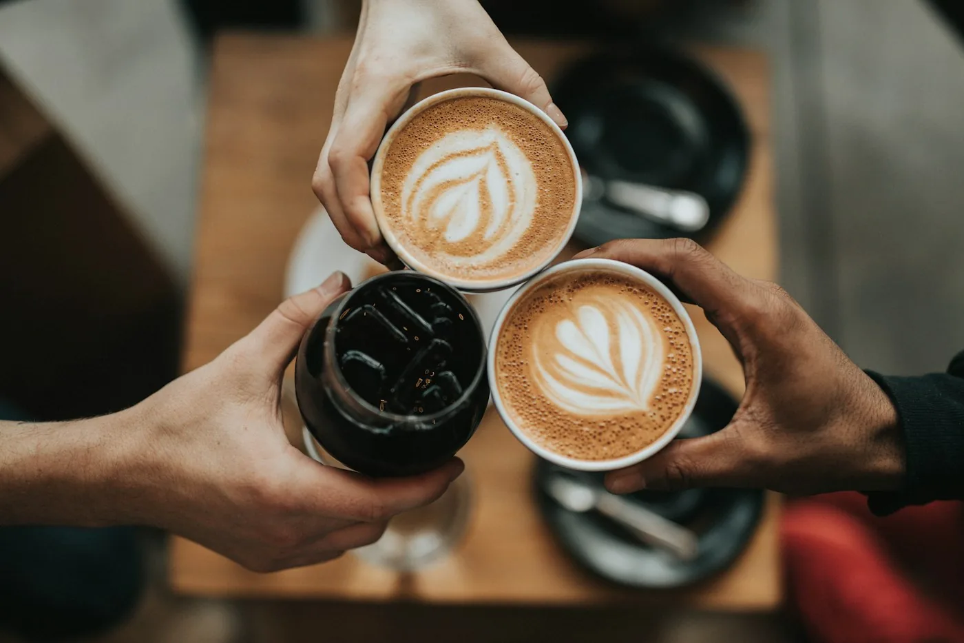 Hands holding cups of coffee above a café table