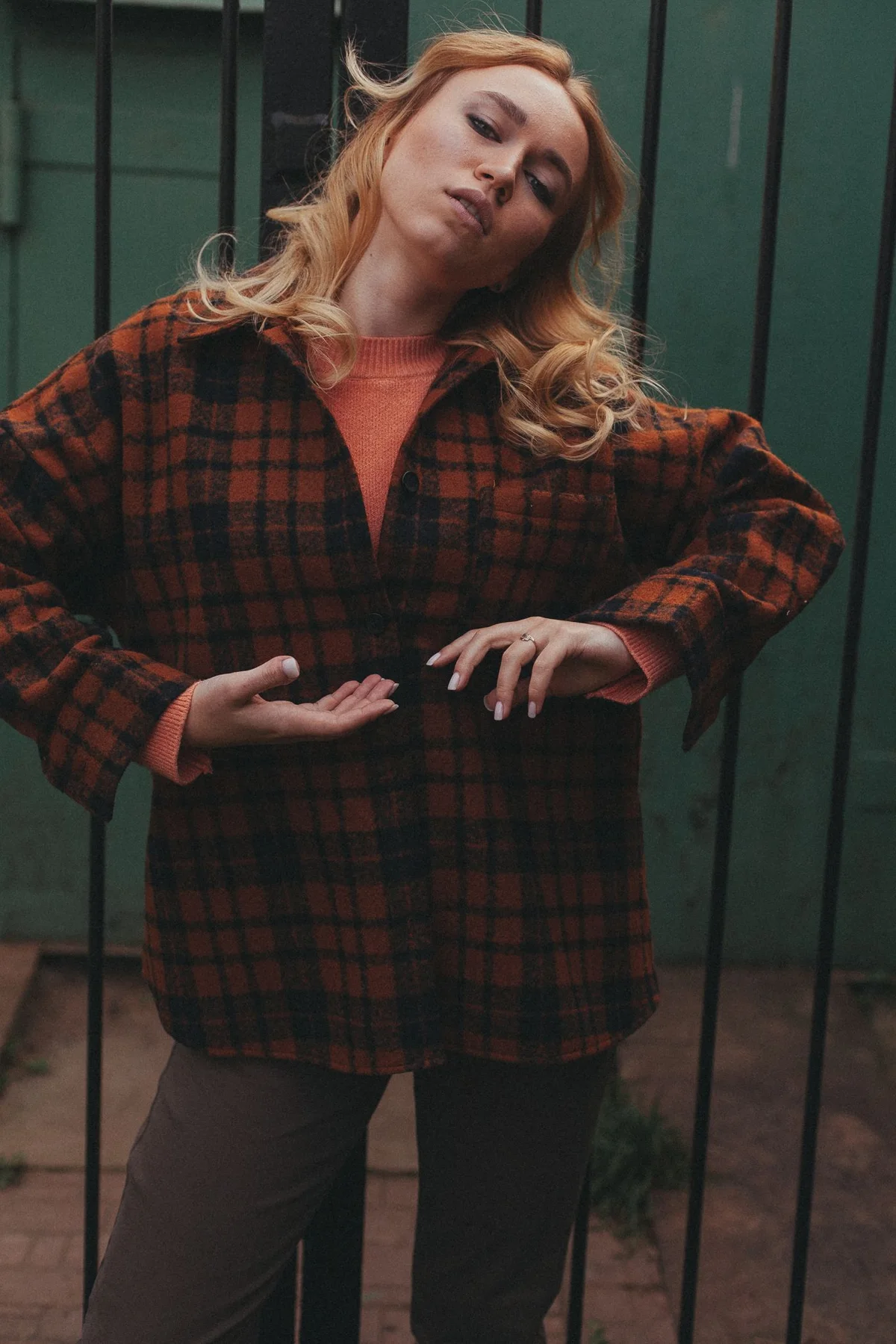 A woman in a belted checked overshirt in front of a dark green door.