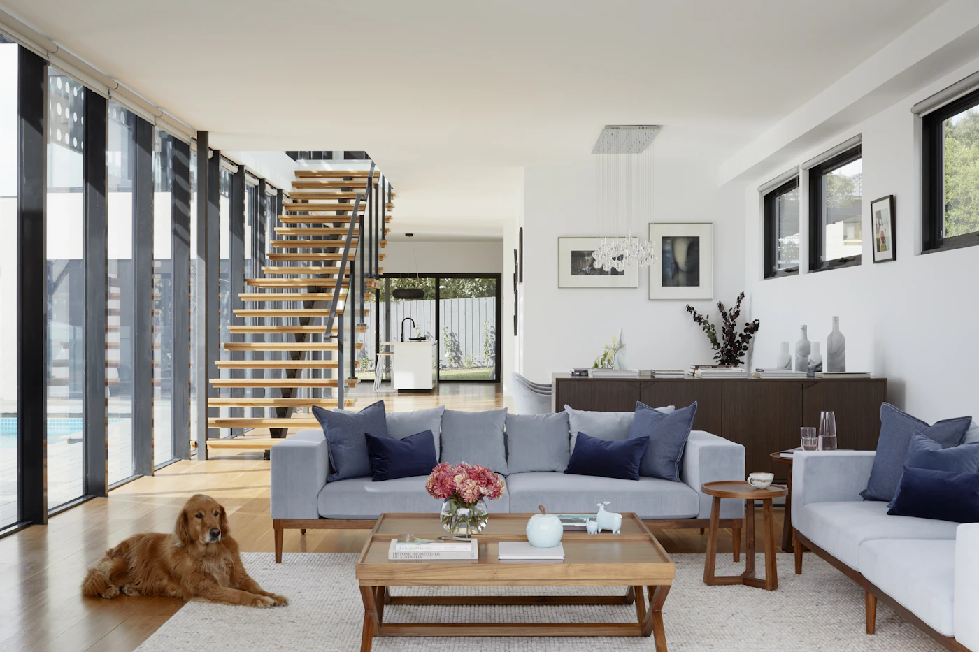 An open living area with pale sofas, a low wooden table and a wooden staircase.