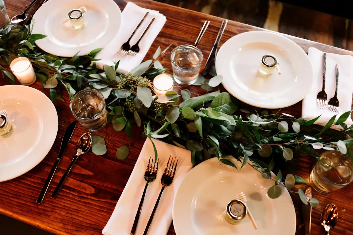 Pale dinner plates and glasses arranged around a wooden dining table.