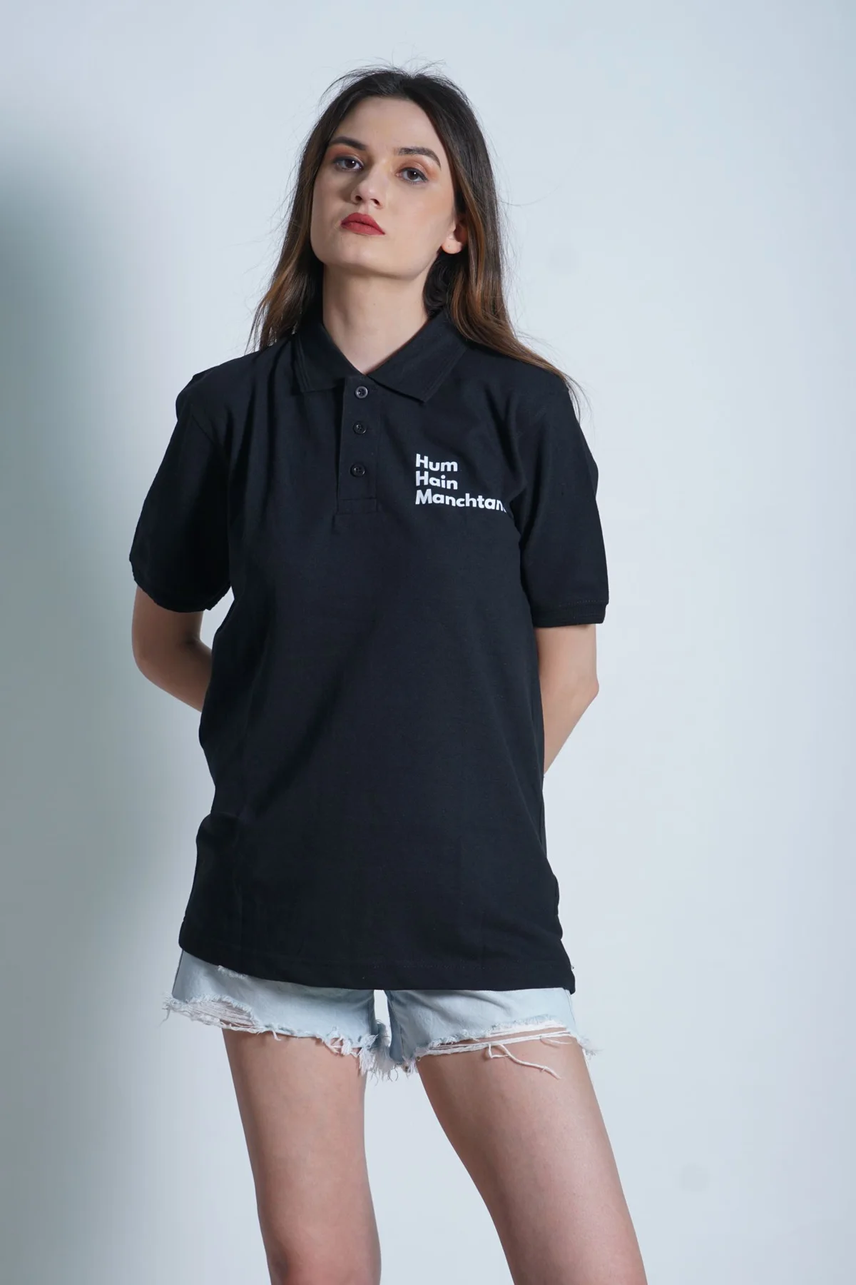 A woman in a dark polo top and pale shorts against a plain background.