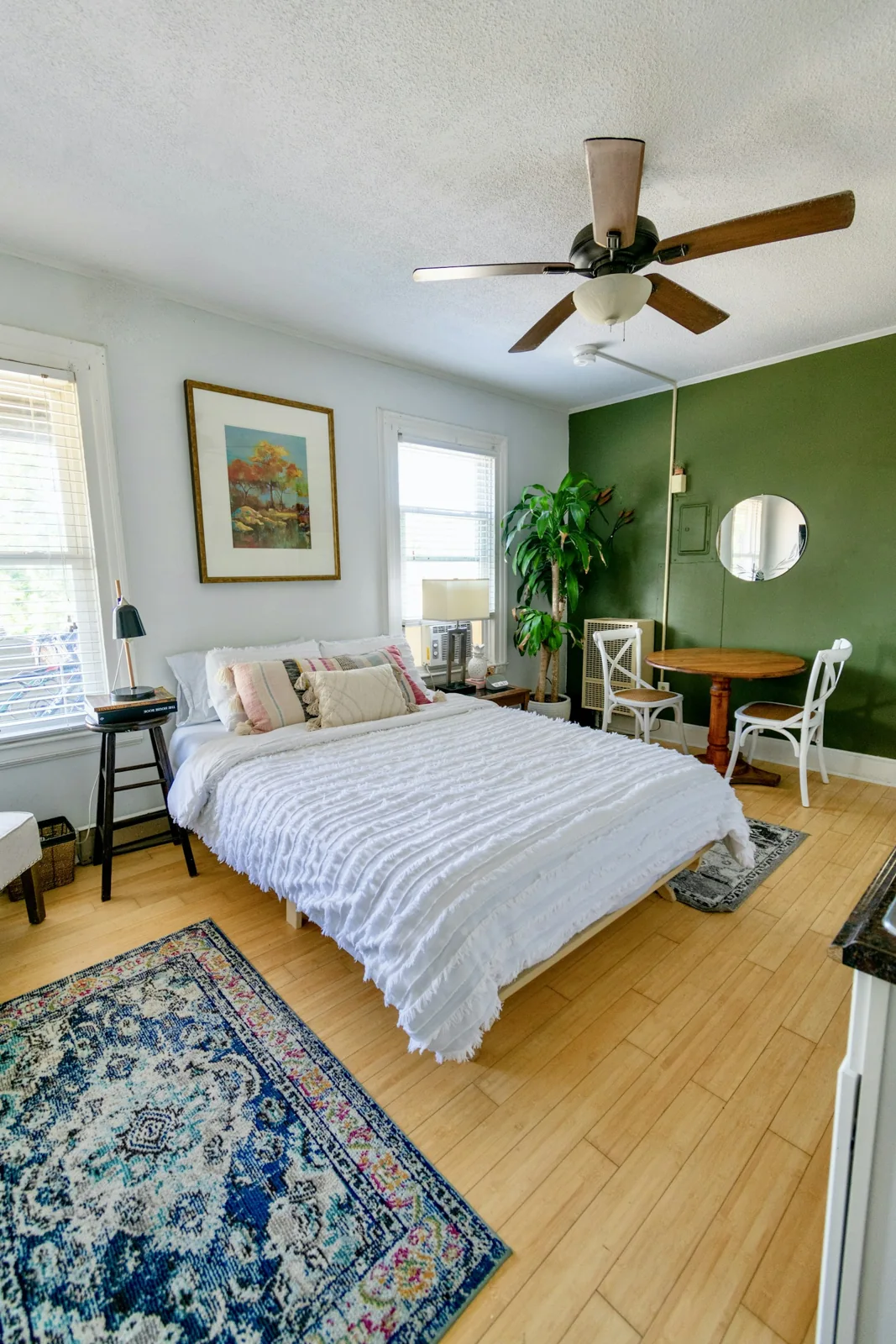 A pale bed beside a green accent wall and wooden floor.