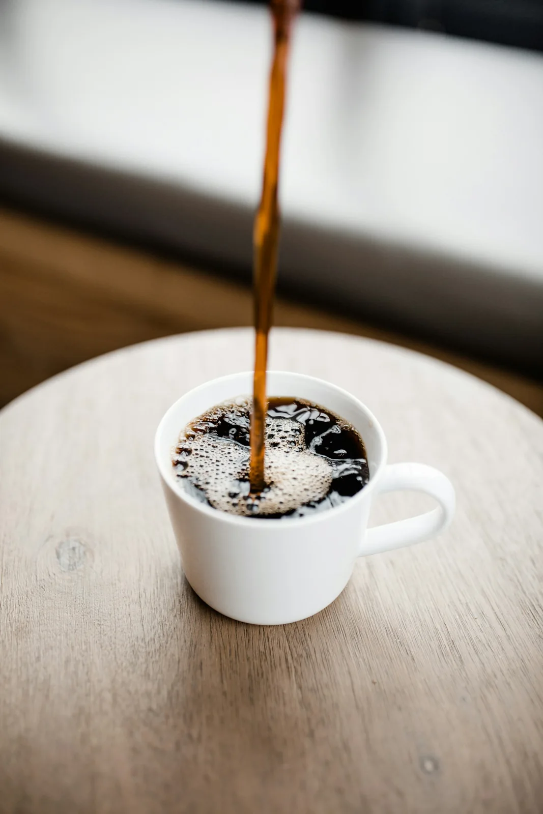 Coffee pouring into a pale cup on a wooden table.