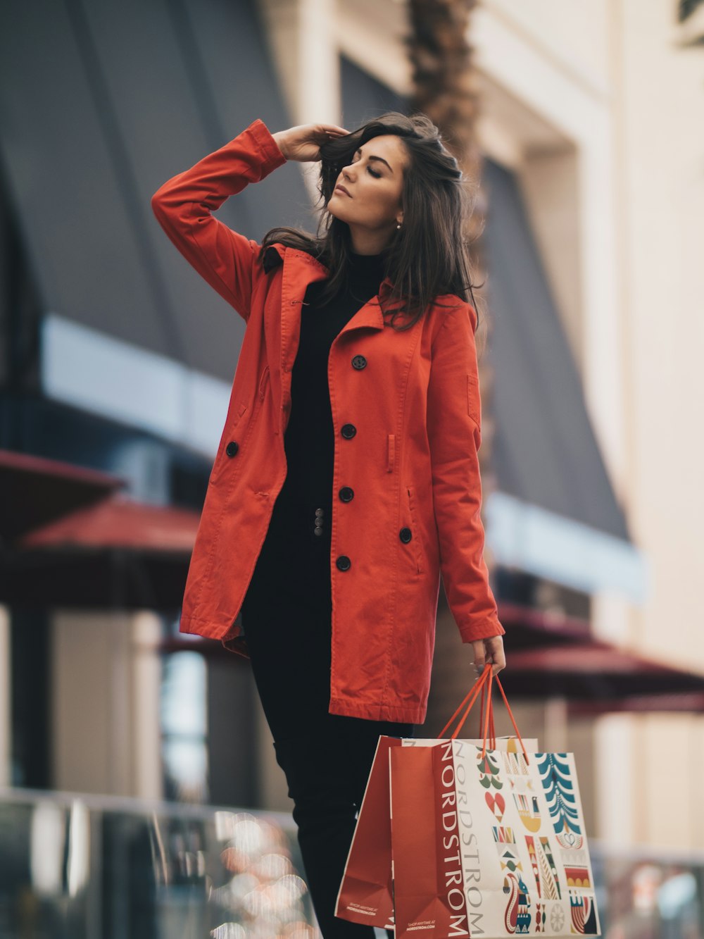 A woman in a red coat over a dark outfit on a city street.