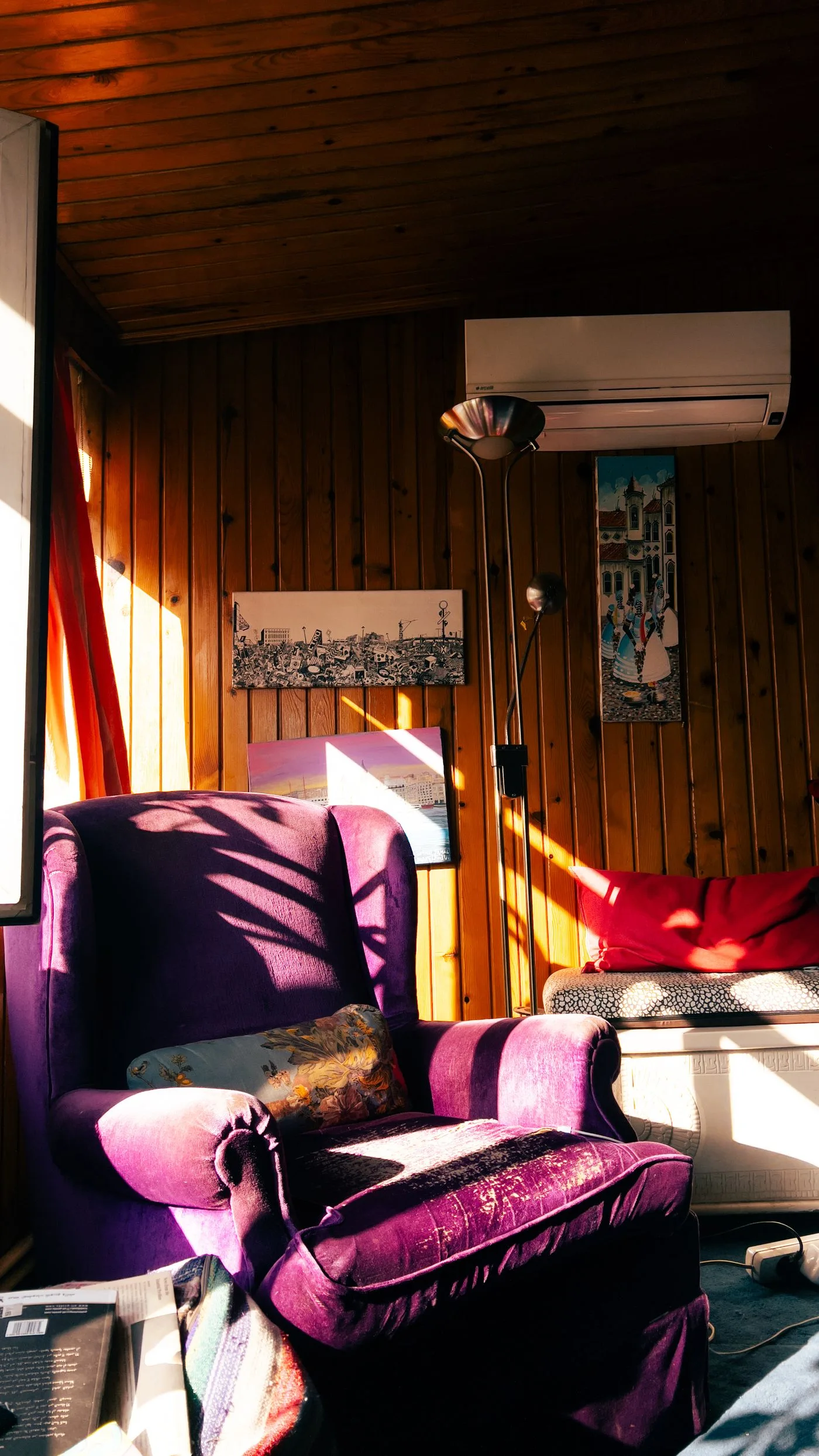 A purple armchair in a warmly lit wooden room with framed wall art.