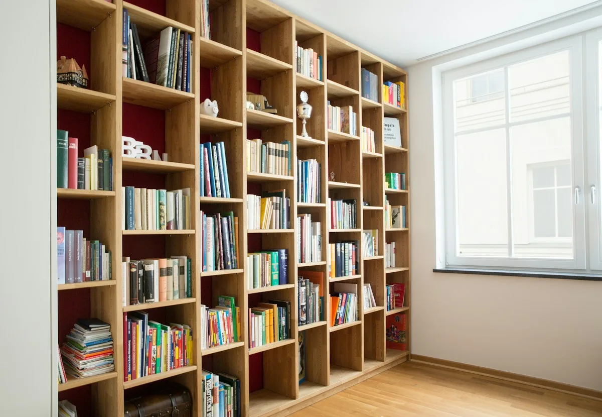 Tall wooden bookcases filled with books beside a bright window.
