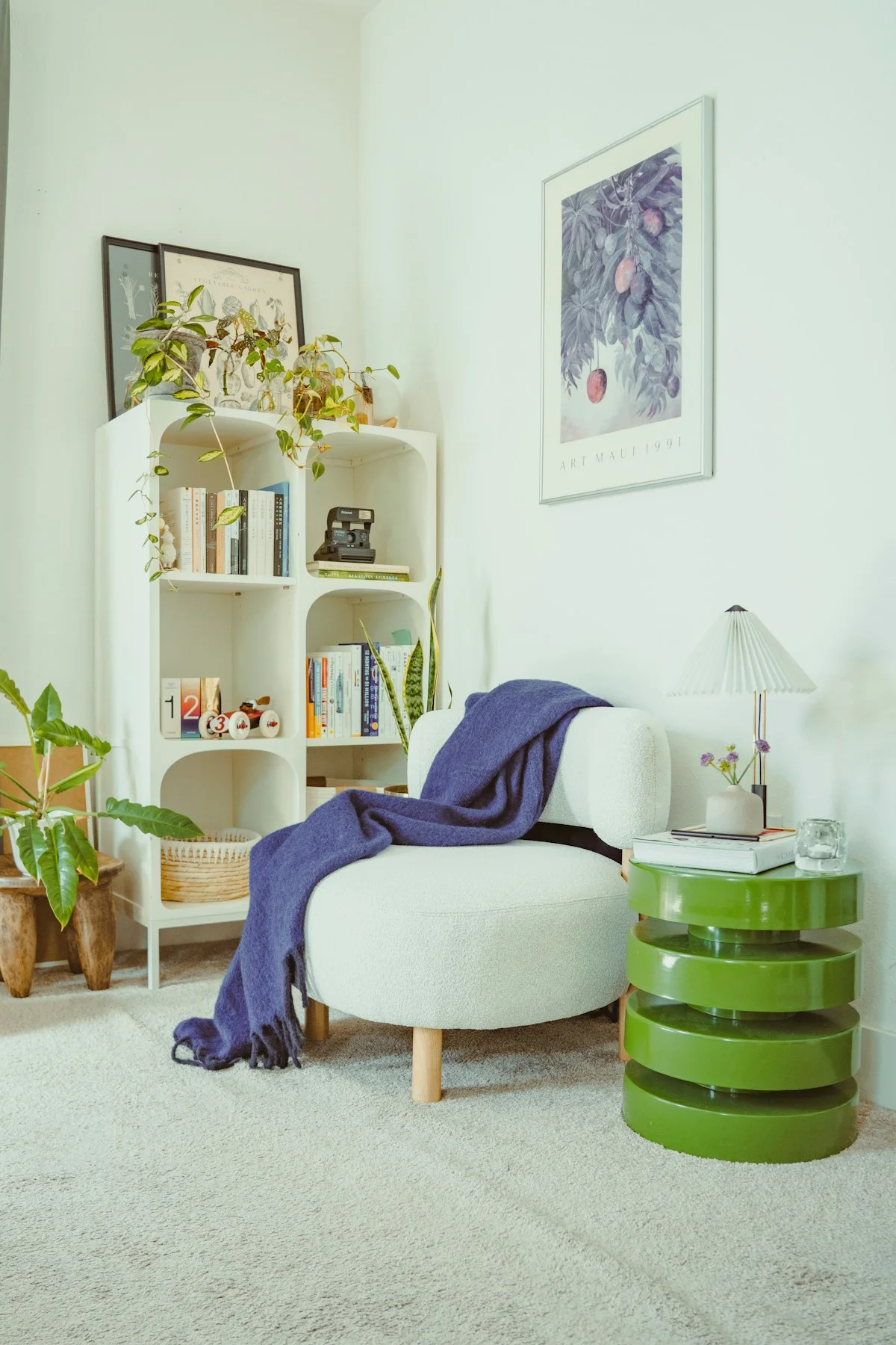 A pale armchair with a blue-purple throw beside green tables and shelving.
