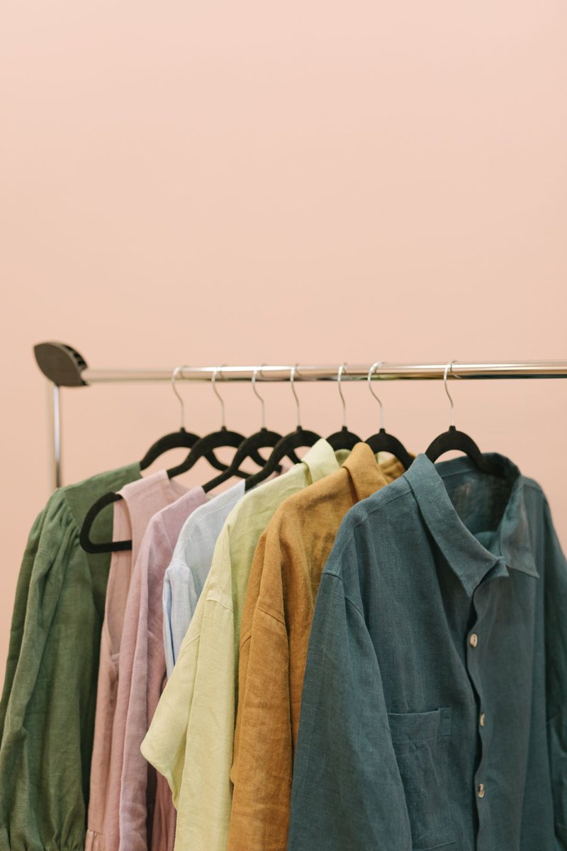 Softly coloured shirts on hangers against a pink wall.