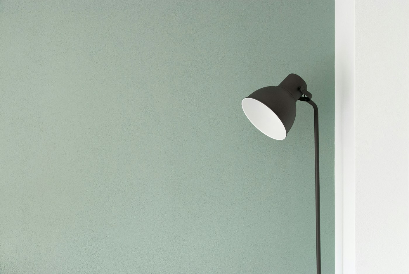 A dark adjustable lamp against a muted green wall.