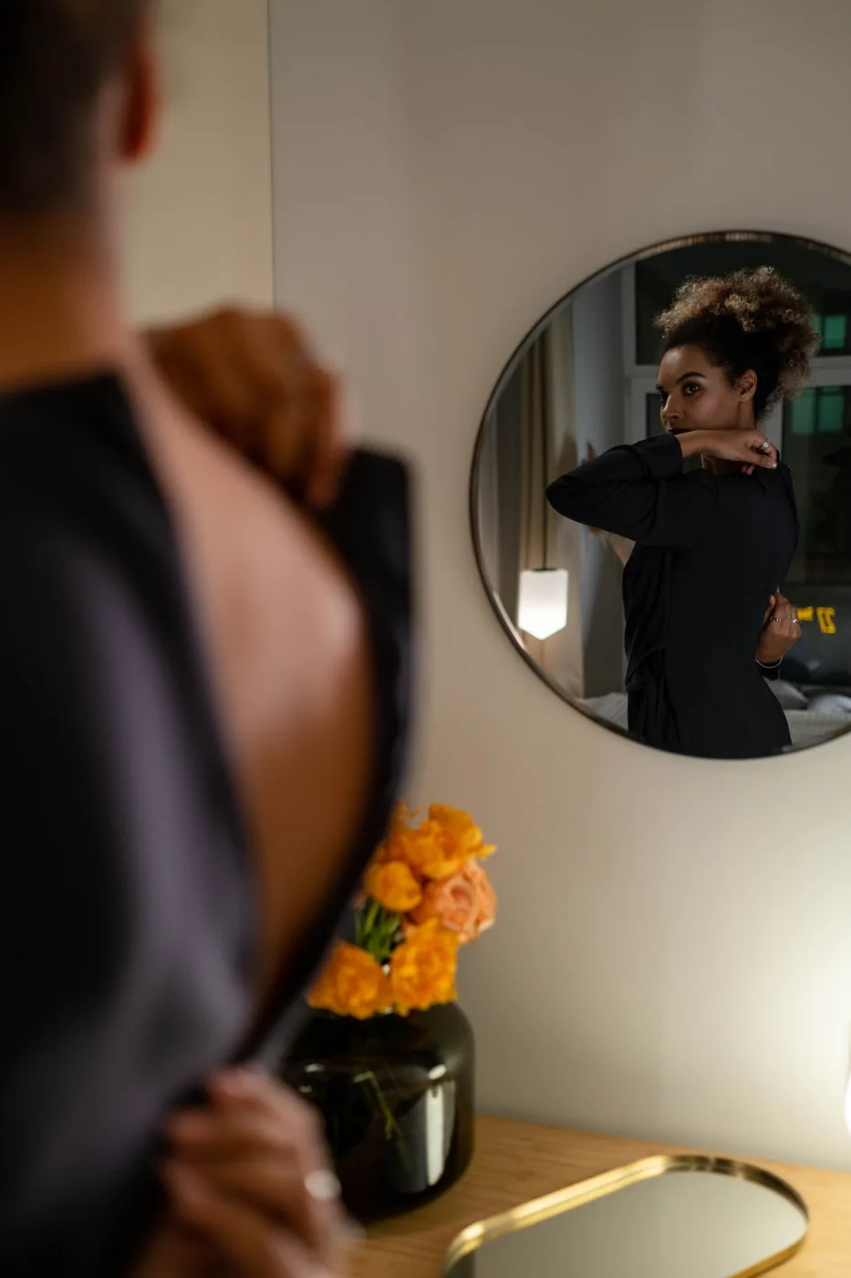 A person in a dark garment reflected in a round wall mirror.