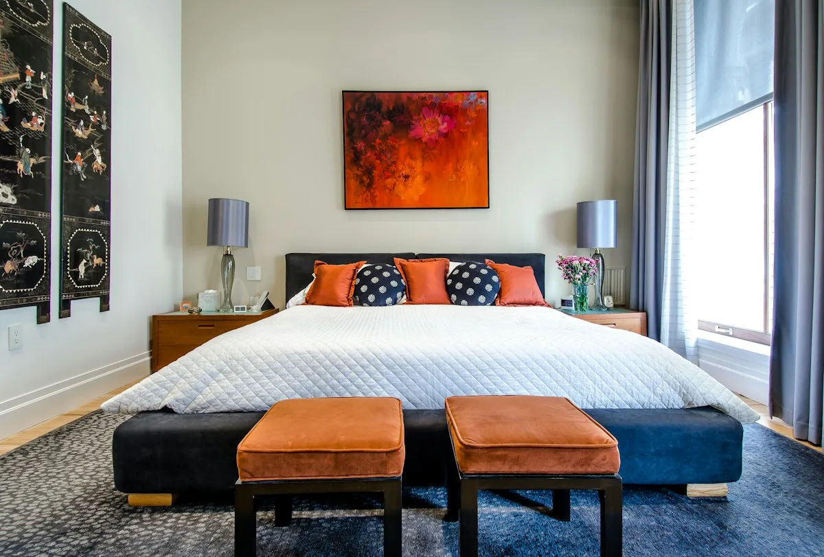 A bedroom with blue-and-white bedding, two upholstered benches and framed wall art.