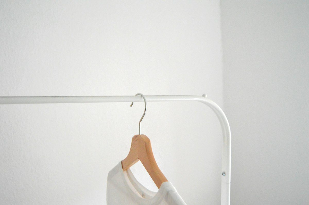 A pale shirt on a wooden hanger against a light wall.