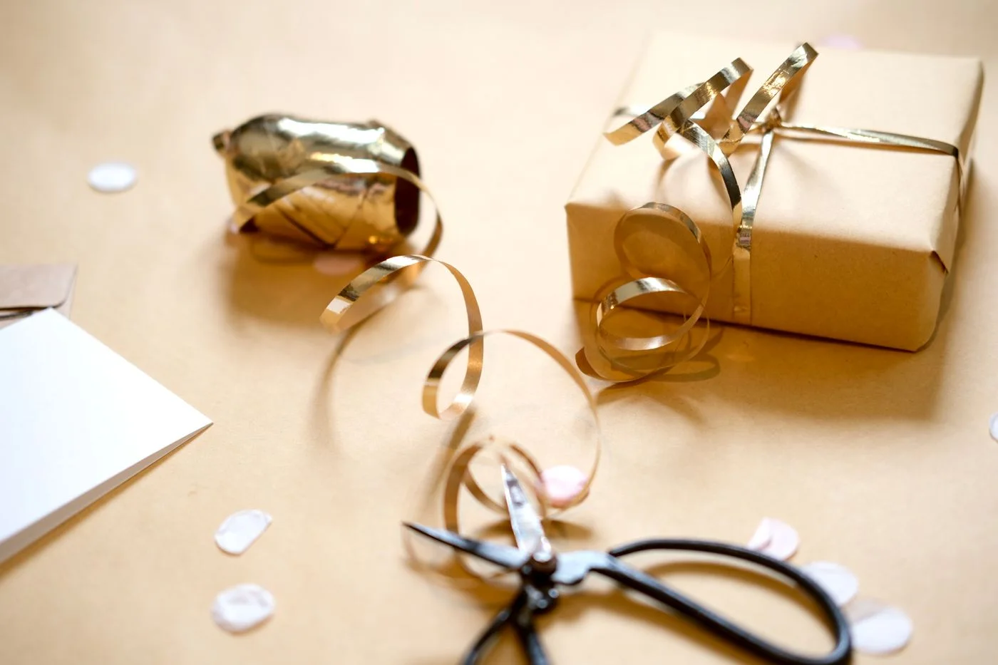 A wrapped gift with gold ribbon beside scissors and wrapping supplies.