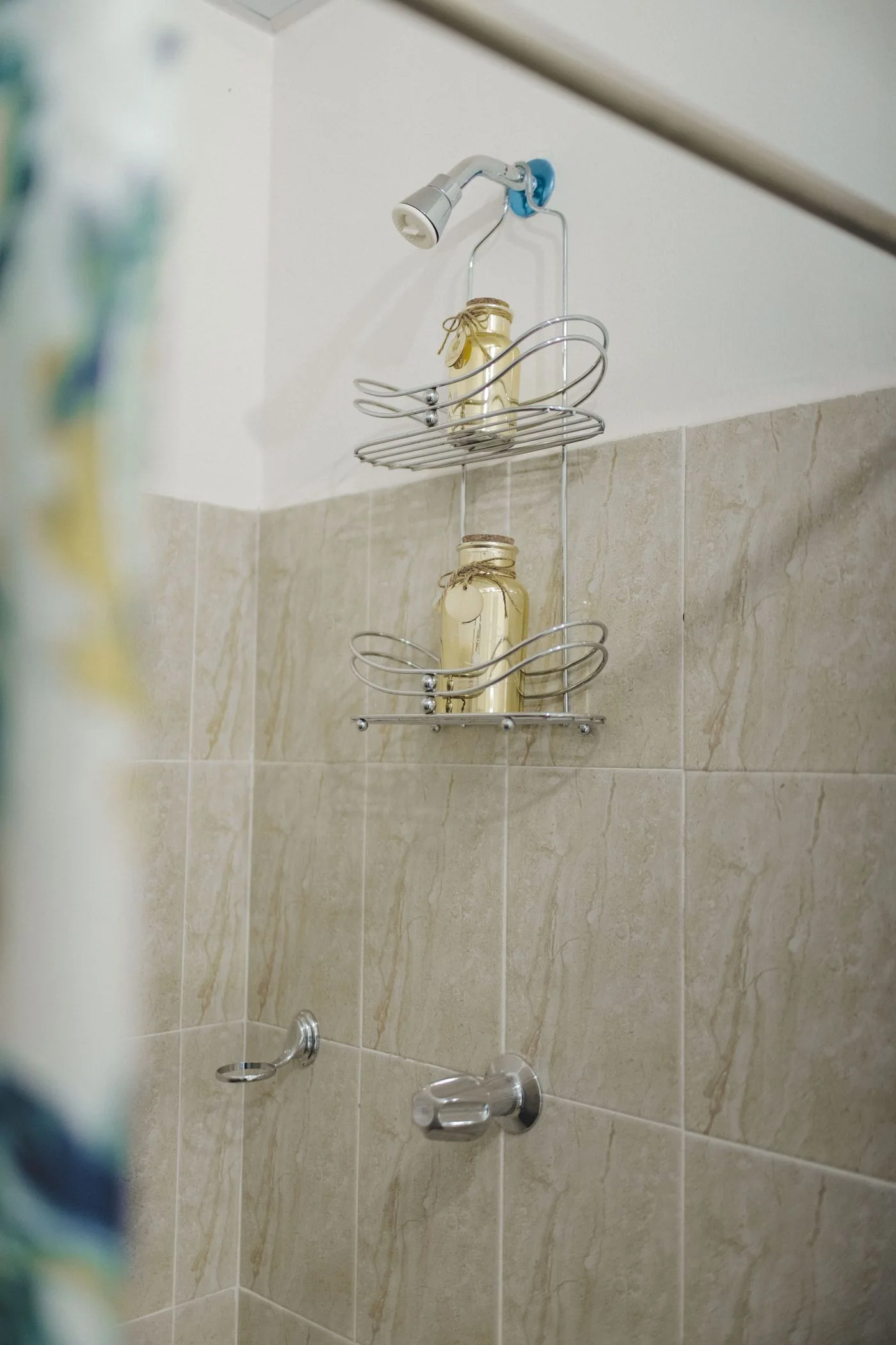Vertical shot of a shower with a sleek wire shelf holding jars against tiled walls.