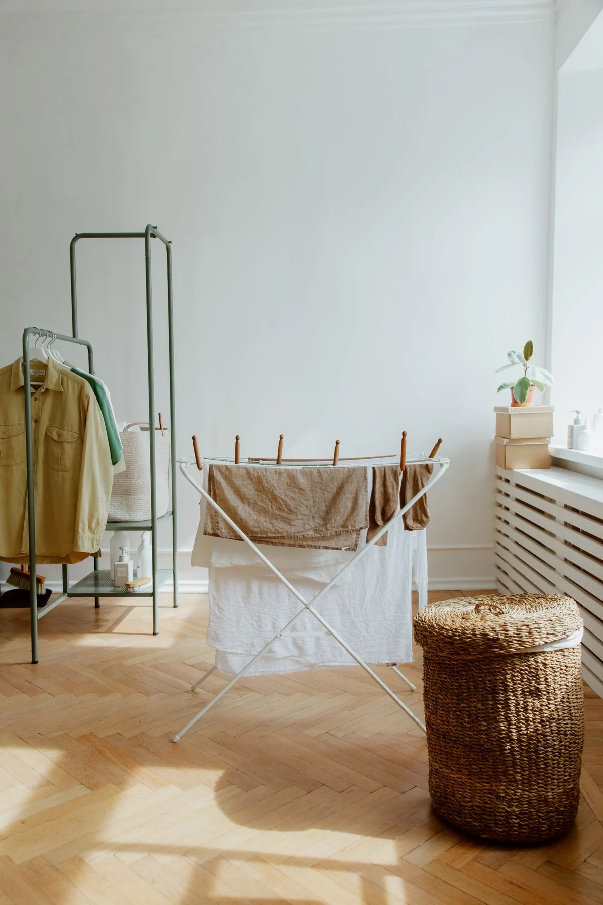 Clothes hanging to dry beside a wicker laundry basket in a sunlit room.