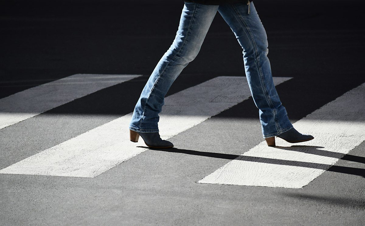 Blue jeans and dark shoes moving across a pedestrian crossing.