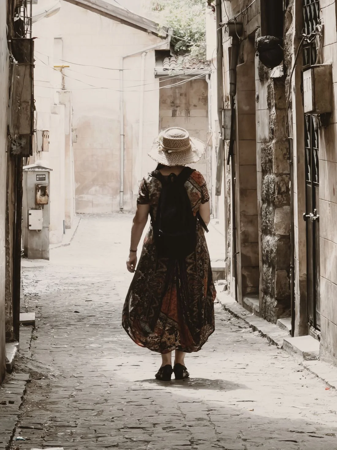 A person in a long patterned dress walking along a narrow street.