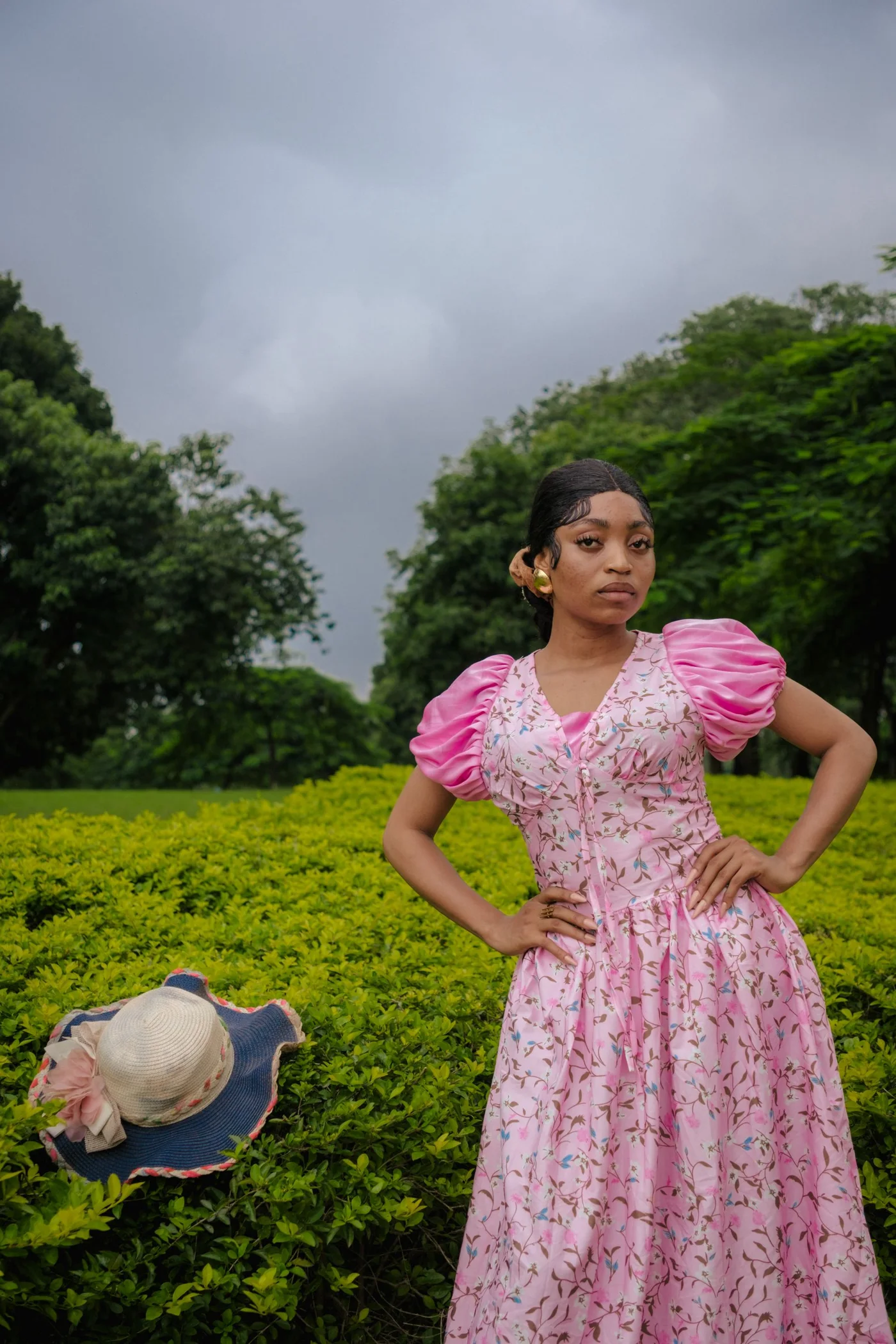 A woman wearing a pink patterned dress beside green plants.