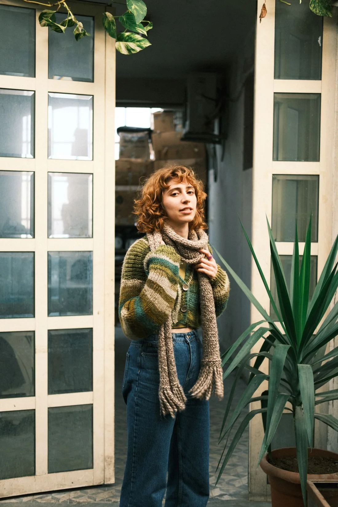 A person wearing a scarf beside a doorway and plants.