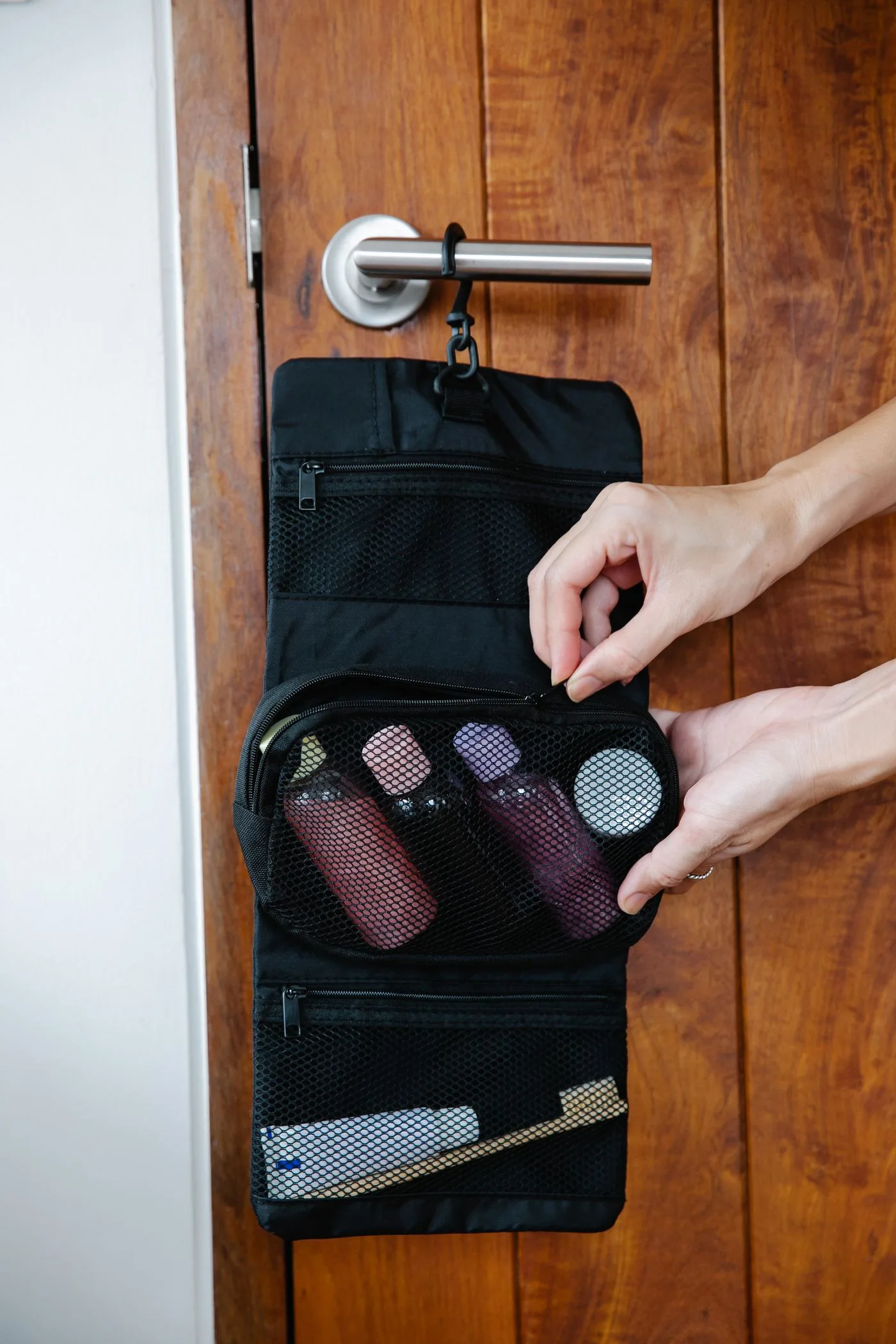 An open dark toiletry bag hanging from a handle on a wooden door.