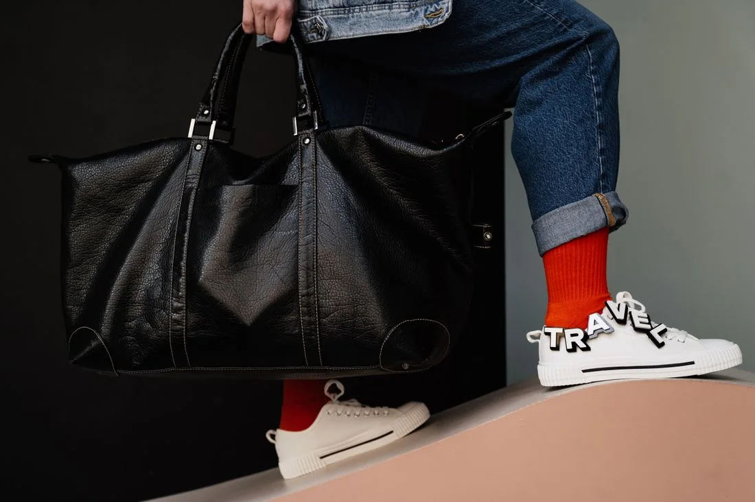 A dark travel bag carried beside cuffed jeans and pale sneakers.